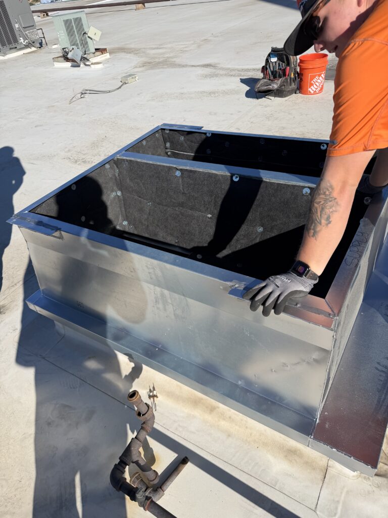 Technician working beside an insulated sheet-metal rooftop curb