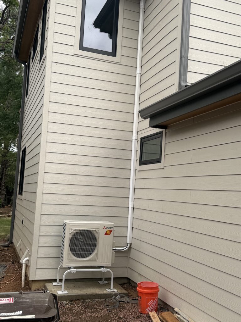 Mitsubishi outdoor heat-pump unit on a raised stand with covered line set