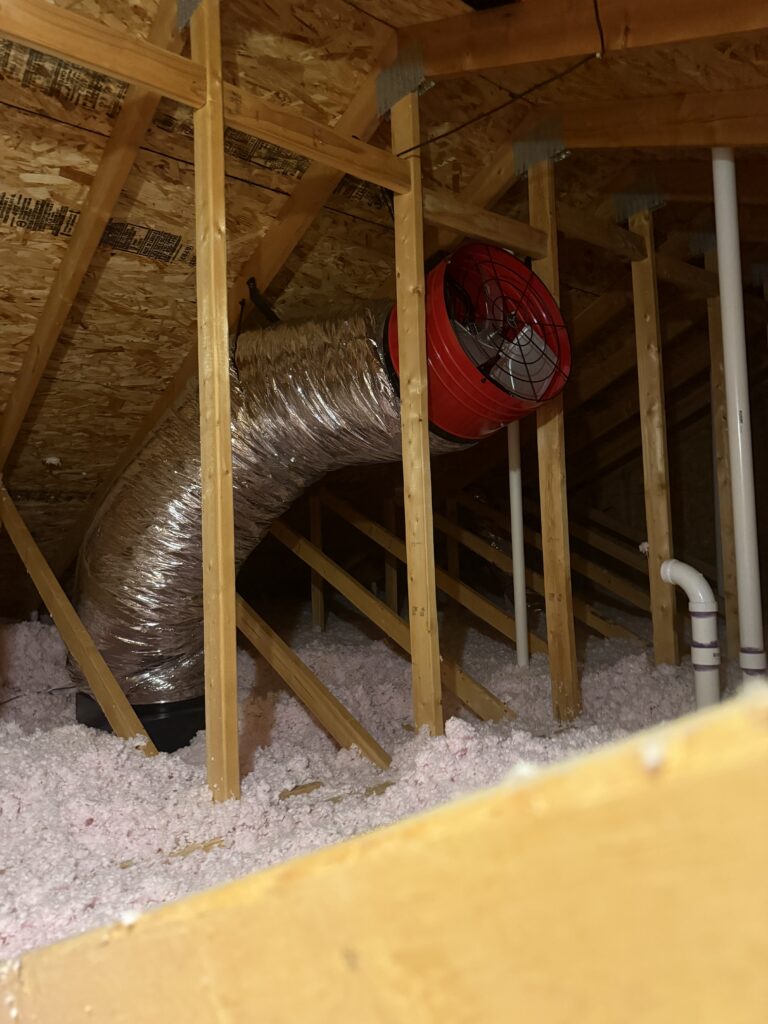 Ducted whole-house fan mounted among attic framing above insulation